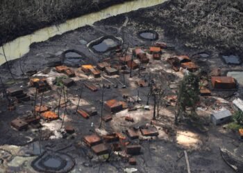 An aerial view of an artisanal oil refining site, with crude pools and burnt drums beside a creek.