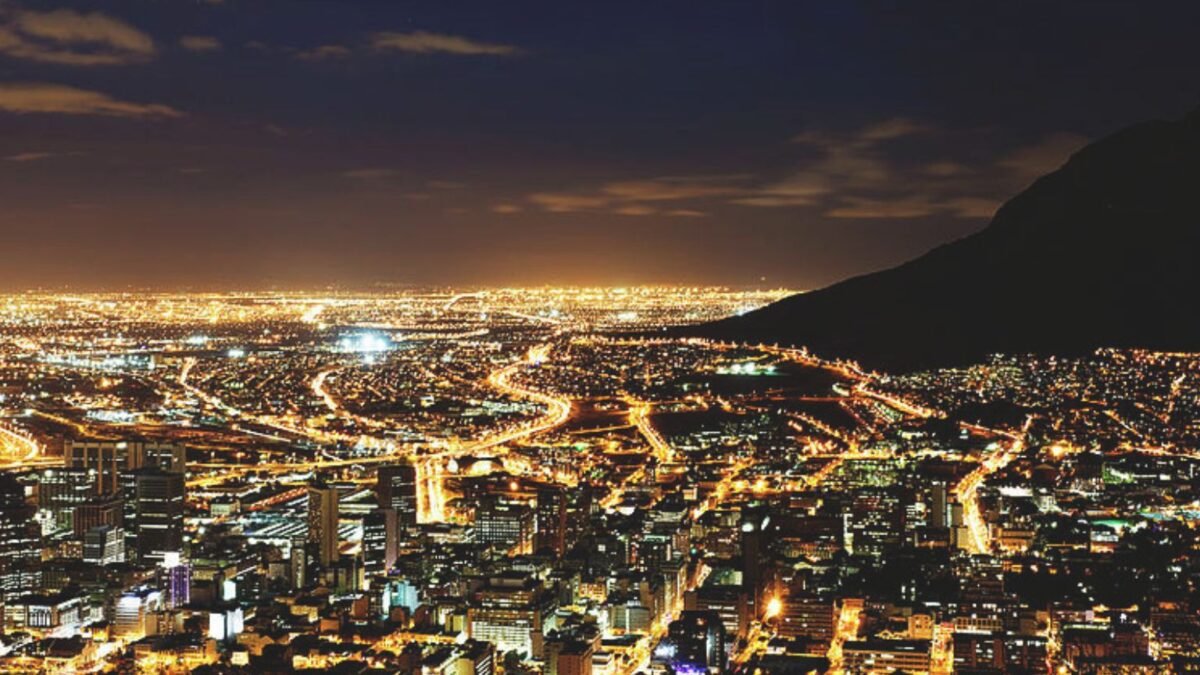 A city skyline lit at night beneath a mountain ridge.