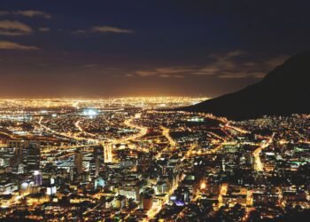 A city skyline lit at night beneath a mountain ridge.