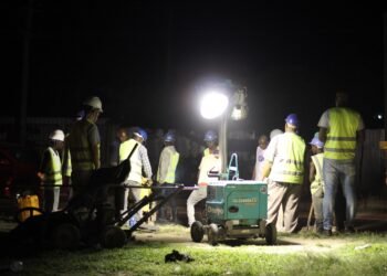 A road construction crew working under floodlights at night in Africa.