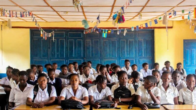 Schoolgirls seated at desks in a classroom hung with international flag bunting.