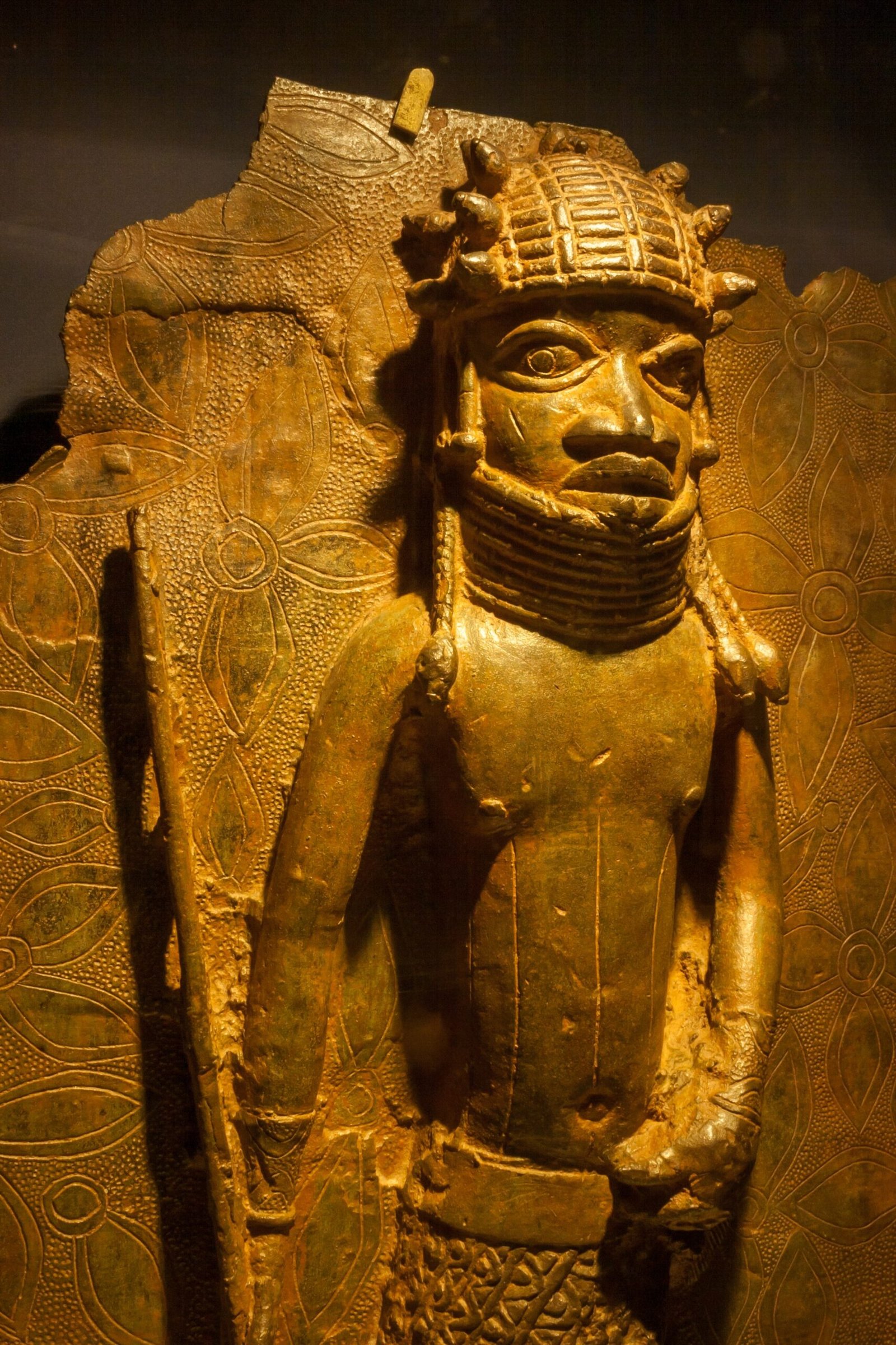 A gilded Benin bronze figure on museum display.